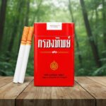 ซองบุหรี่กรองทิพย์ 90 แบบซองอ่อนสีแดงเอกลักษณ์ พร้อมมวนบุหรี่ก้นกรองสีส้ม วางบนโต๊ะไม้ในป่า