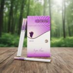 กล่องบุหรี่ Oris Grape สีม่วงขาวดีไซน์ทันสมัย วางบนโต๊ะไม้ฉากหลังป่าไม้สีเขียว